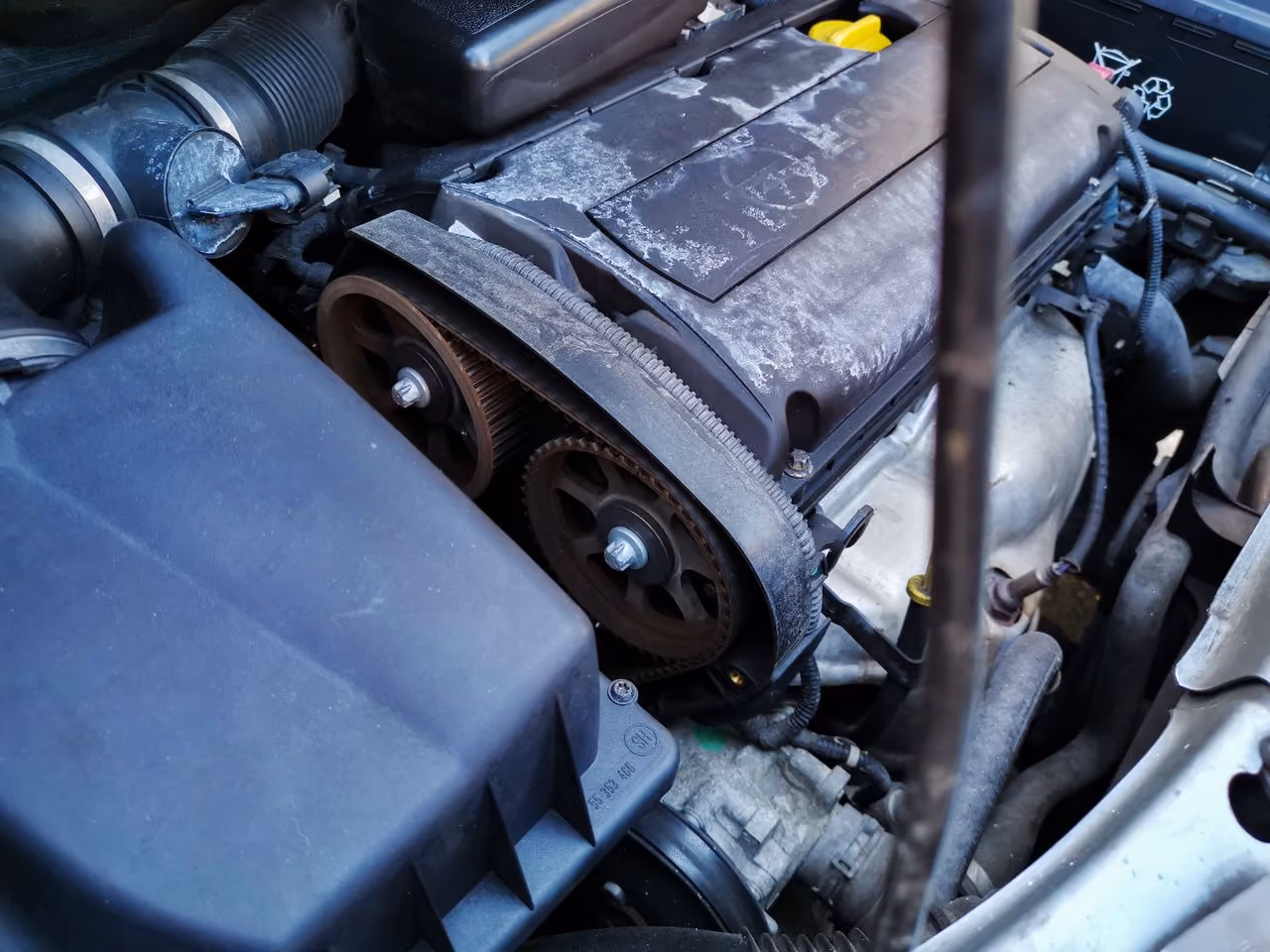 Close-up of a car engine showing a worn timing belt wrapped around two gears.