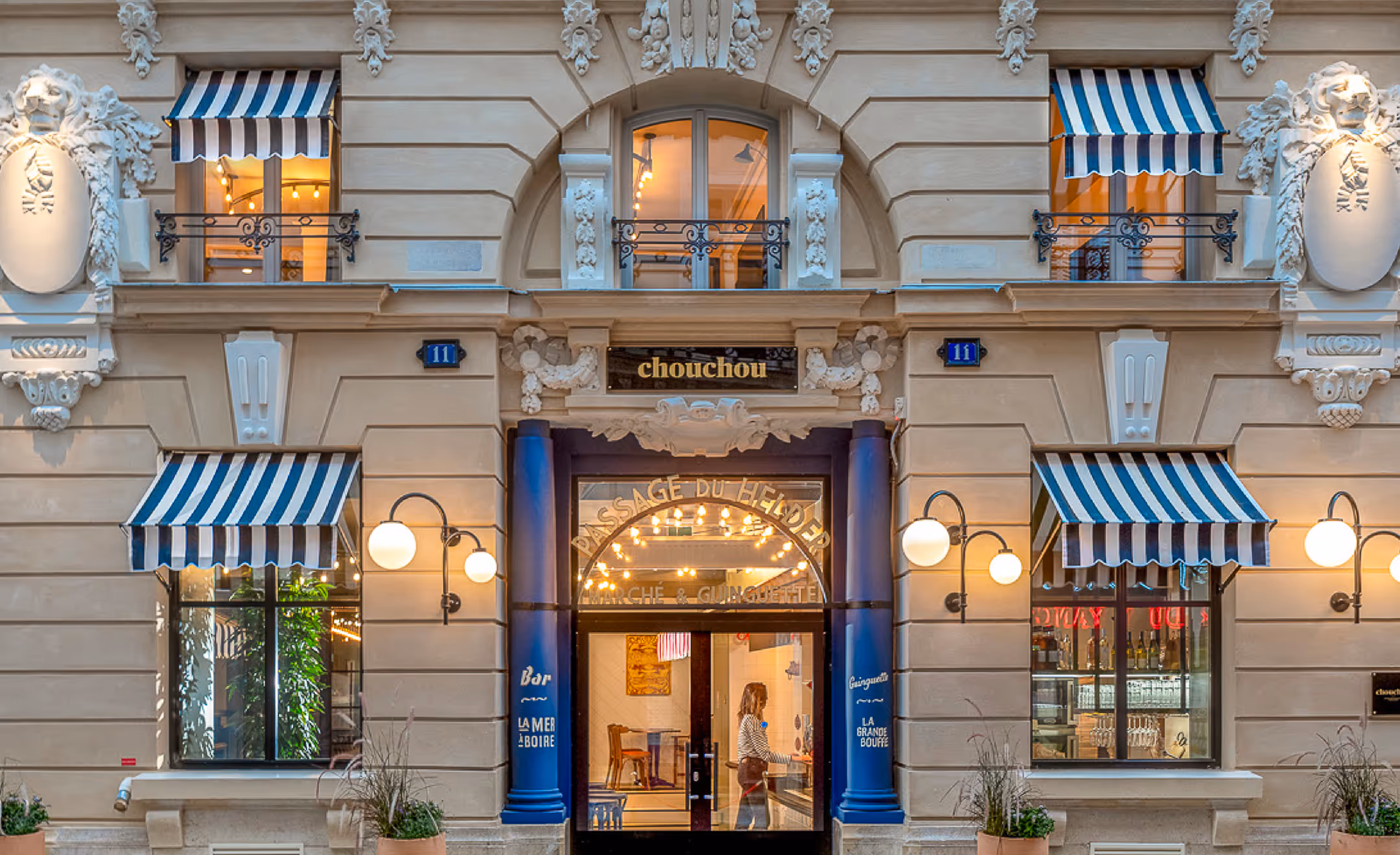 Façade parisienne du restaurant Chouchou avec stores rayés bleu et blanc, signée Hospitality Family.