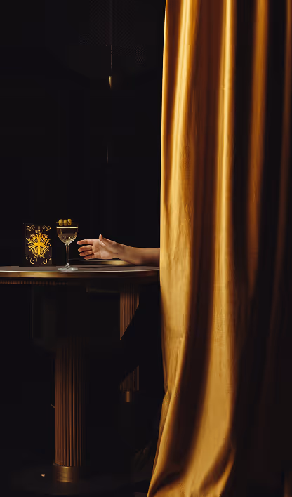 Main tendue près d'un cocktail derrière un rideau doré, ambiance signée Hospitality Family.
