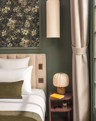 Chambre au décor vert et beige avec lampe champignon et table de chevet, signée Hospitality Family.