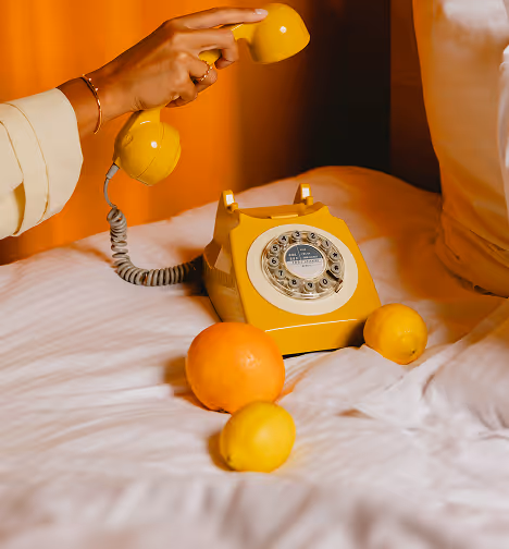 Téléphone vintage jaune sur un lit avec agrumes, ambiance signée Hospitality Family.