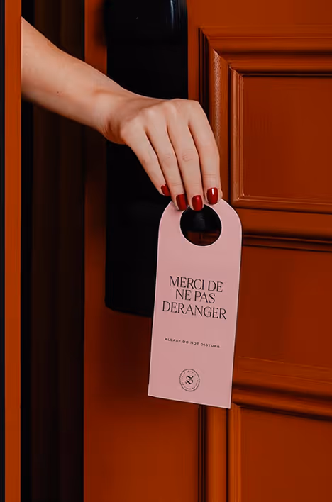 Main accrochant une pancarte « Ne pas déranger » sur une porte, signée Hospitality Family.