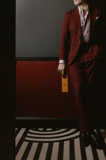 Homme en costume bordeaux tenant une pancarte de porte, ambiance signée Hospitality Family.