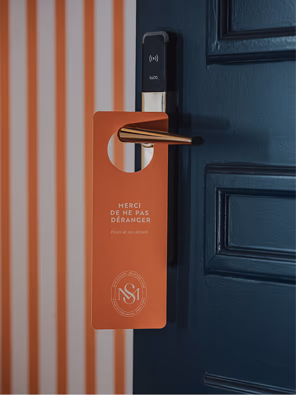 Pancarte « Ne pas déranger » orange sur une porte bleu marine, signée Hospitality Family.