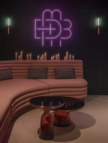 Salon feutré avec canapé rose, bougies et enseigne néon HDB, signé Hospitality Family.