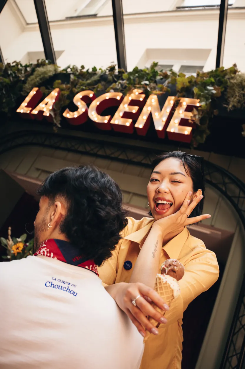 Femme riante tenant une glace face à un homme, sous l'enseigne La Scène du restaurant Chouchou.