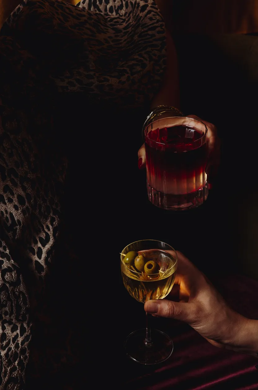 Deux mains présentant un cocktail rouge et un martini aux olives, ambiance signée Hospitality Family.