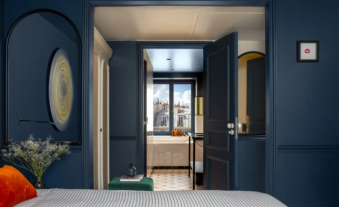 Chambre bleu nuit du restaurant Chouchou avec vue sur la salle de bain et les toits parisiens, signée Hospitality Family.