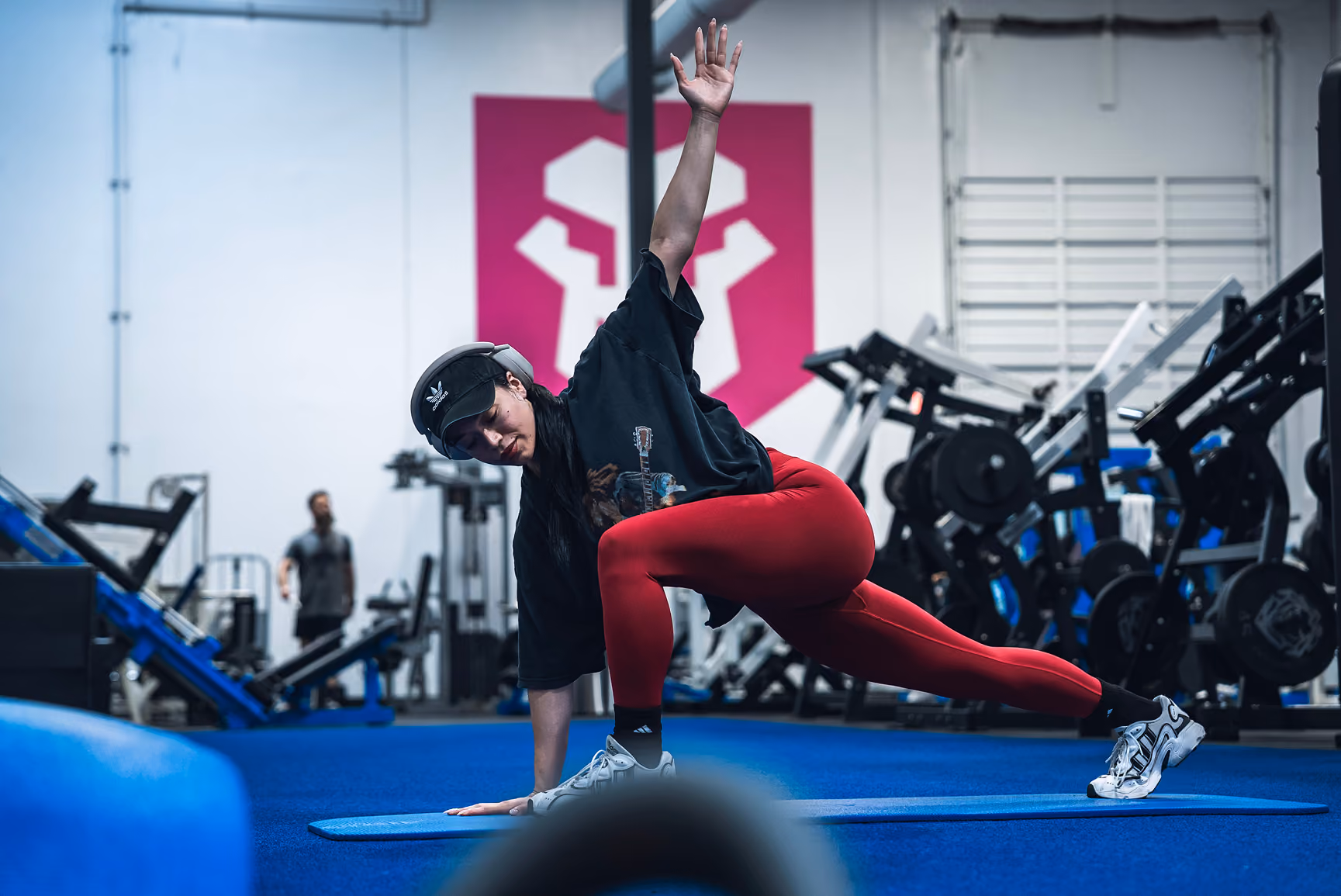 Woman in red leggings stretching with one hand on mat and other raised in gym.