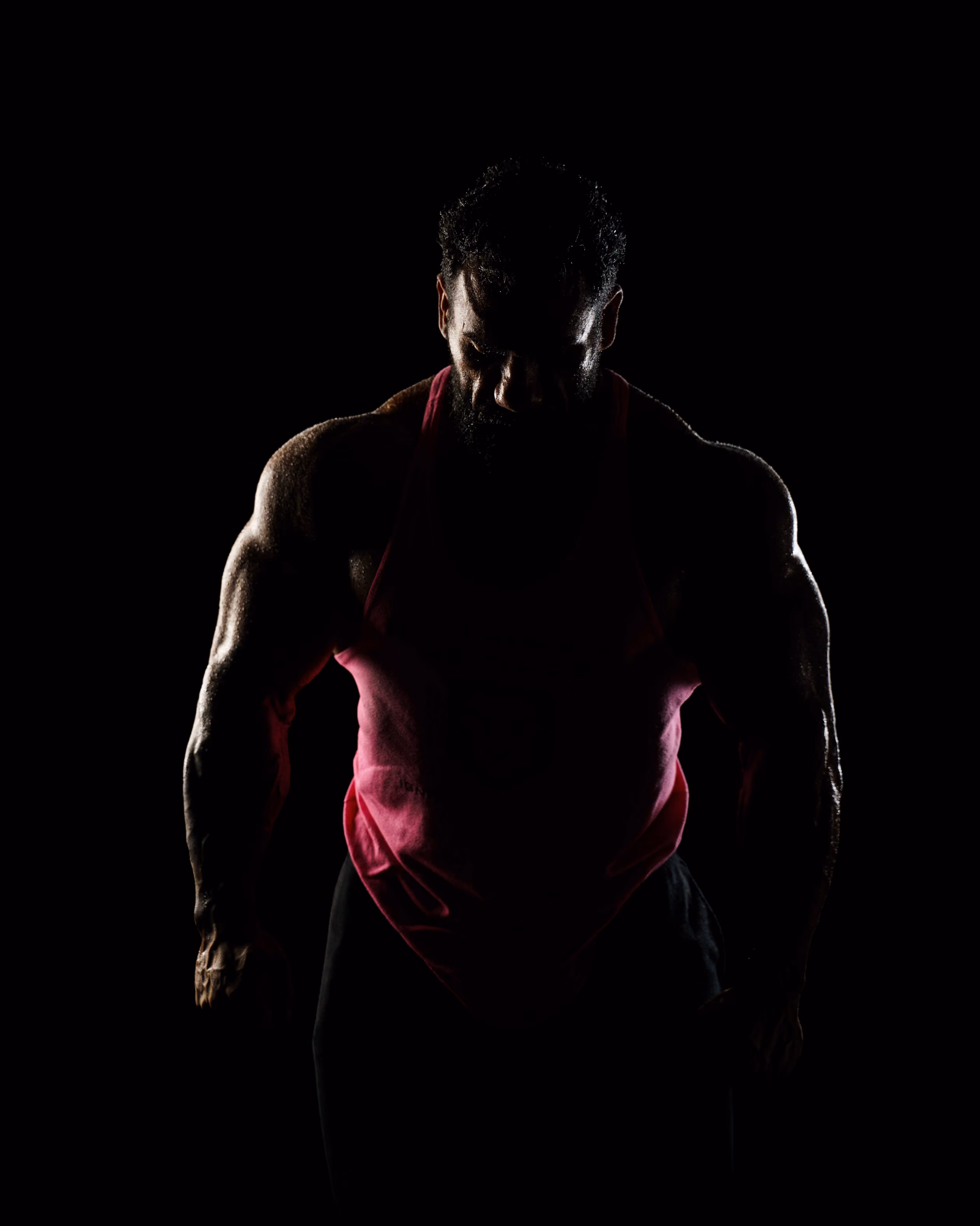Silhouetted muscular man wearing a pink tank top against a black background.