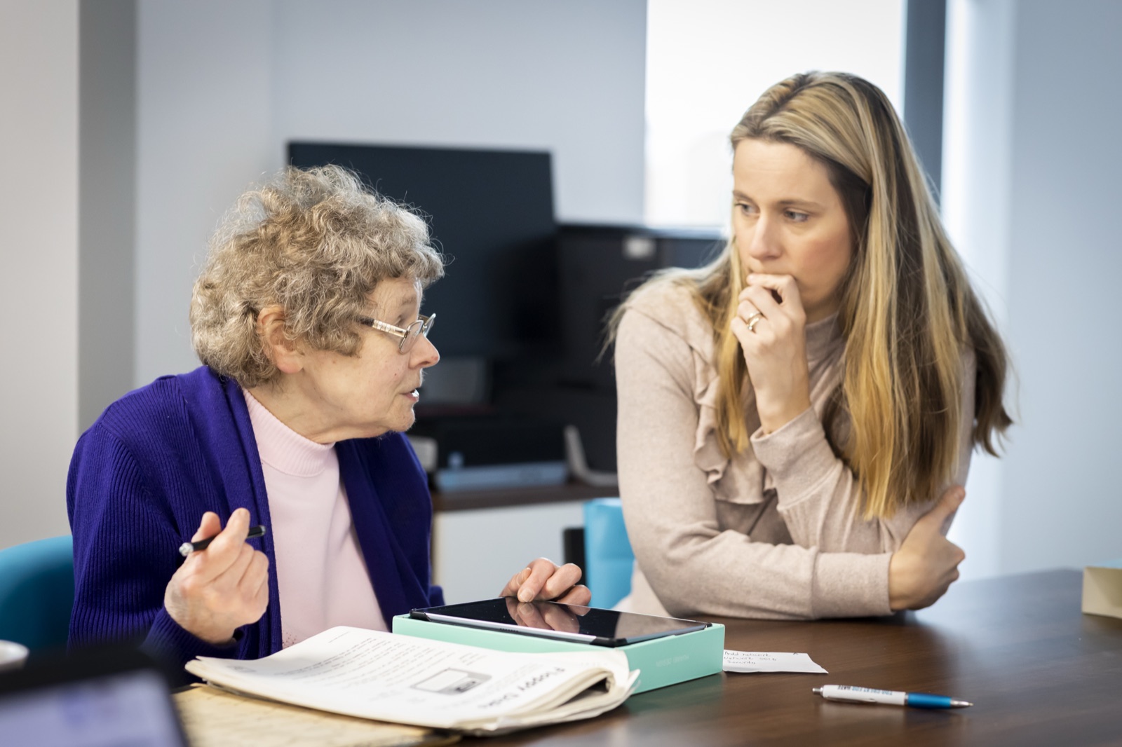 An older woman with a tablet talking through her notes with a younger adviser