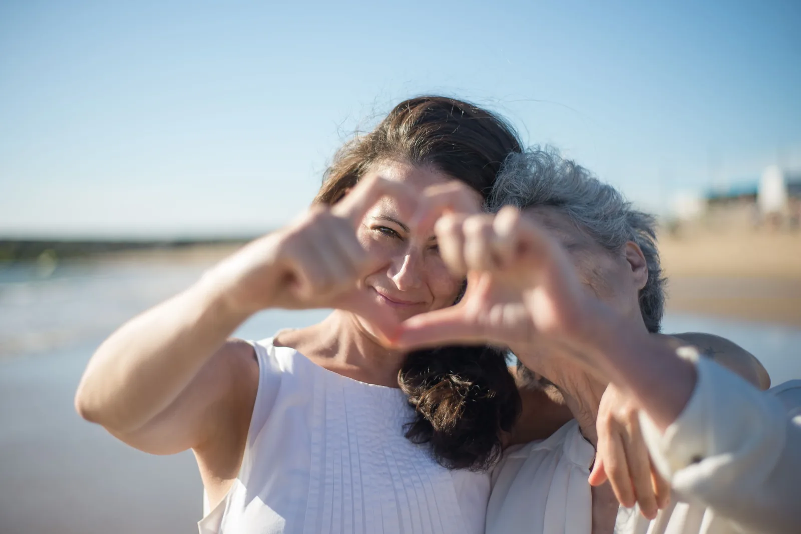 A caregiver and a smiling elderly woman holding hands together in a garden