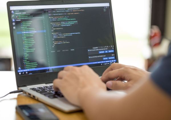 Osoba pisząca kod na laptopie z widocznym edytorem tekstu i kodem programu.
