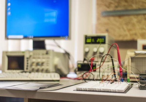Laboratoryjny stół z urządzeniami do testów elektronicznych i płytką prototypową z przewodami.