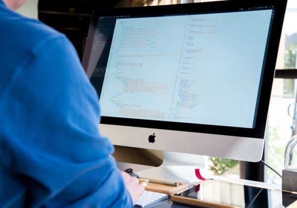 Osoba pisząca kod na komputerze iMac na biurku z klawiaturą i tabletem.