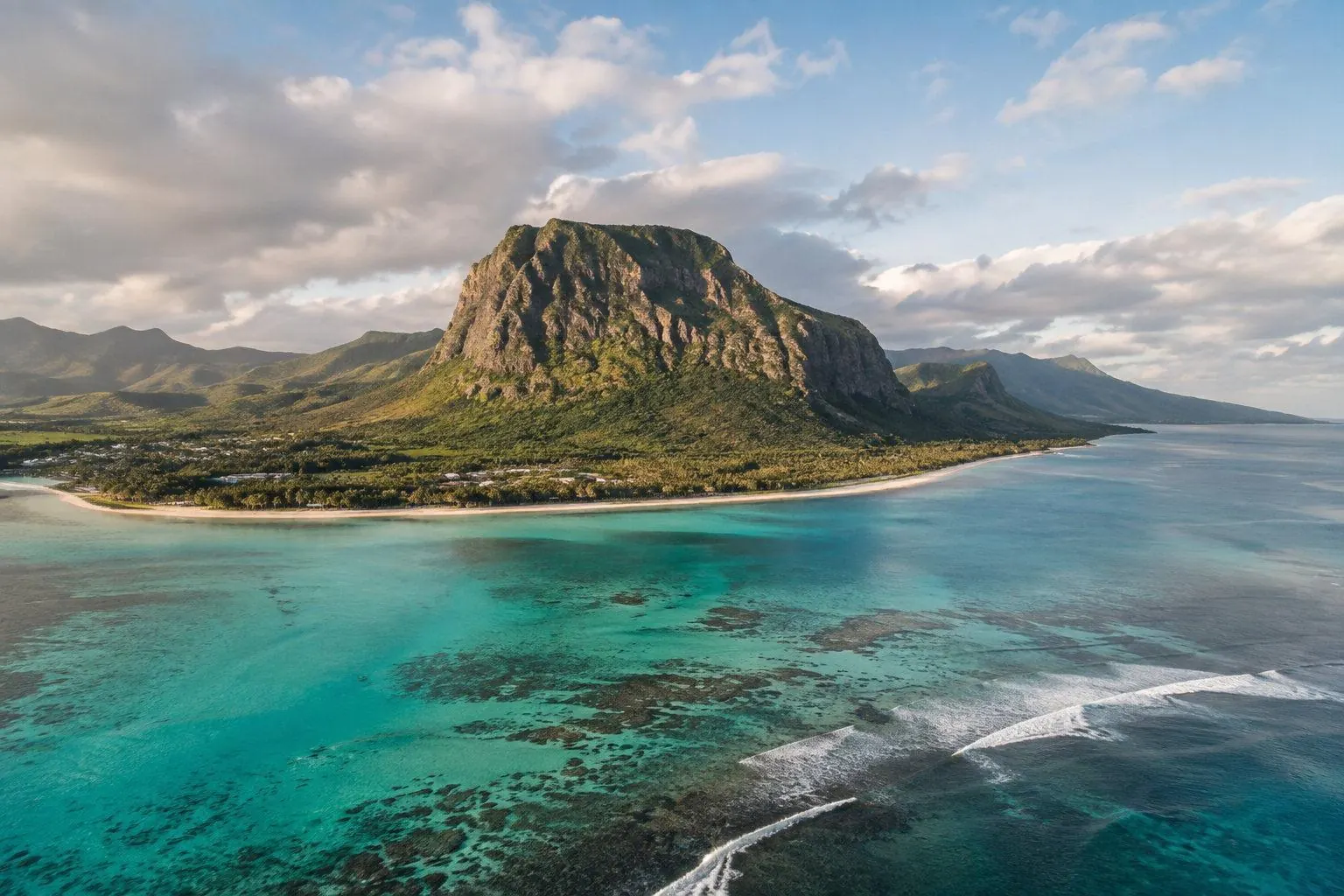 Aerial view of a green mountain headland ringed by turquoise reef water in Mauritius