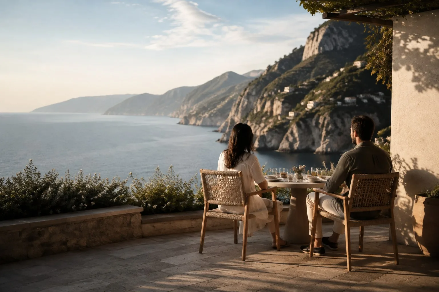 A couple at a terrace table above the Amalfi coastline at golden hour