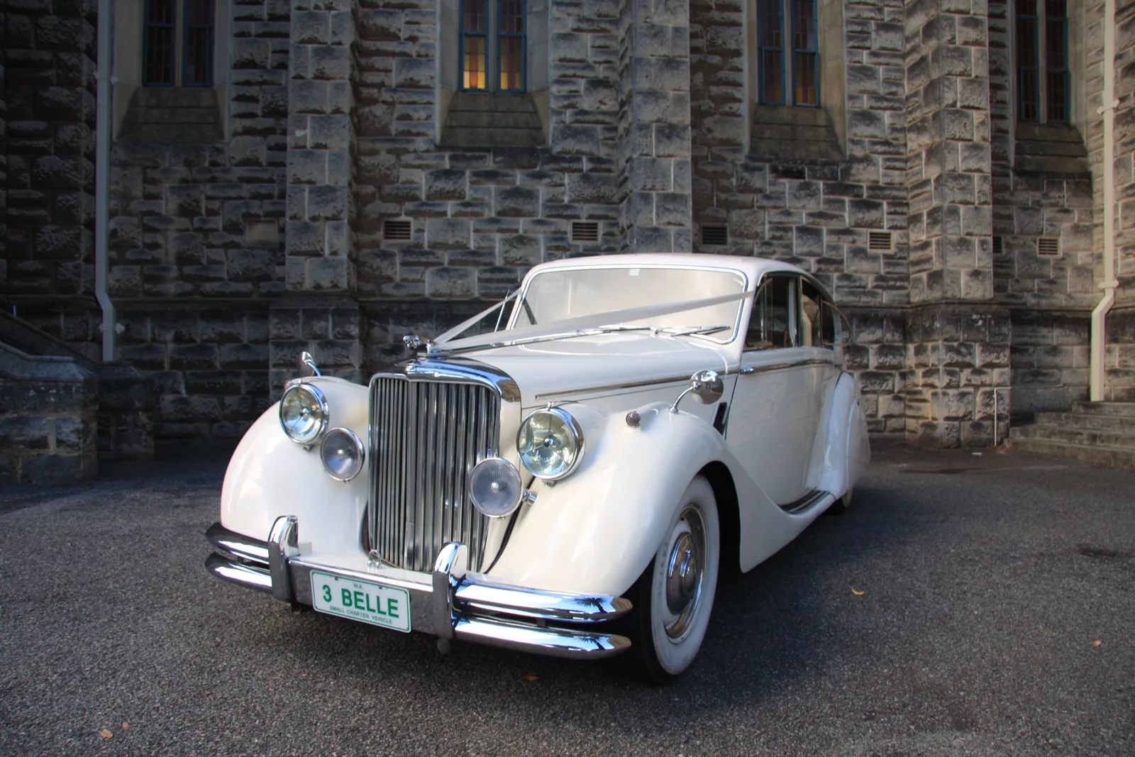 Classic Jaguar sedan wedding car outside a Perth stone church at dusk