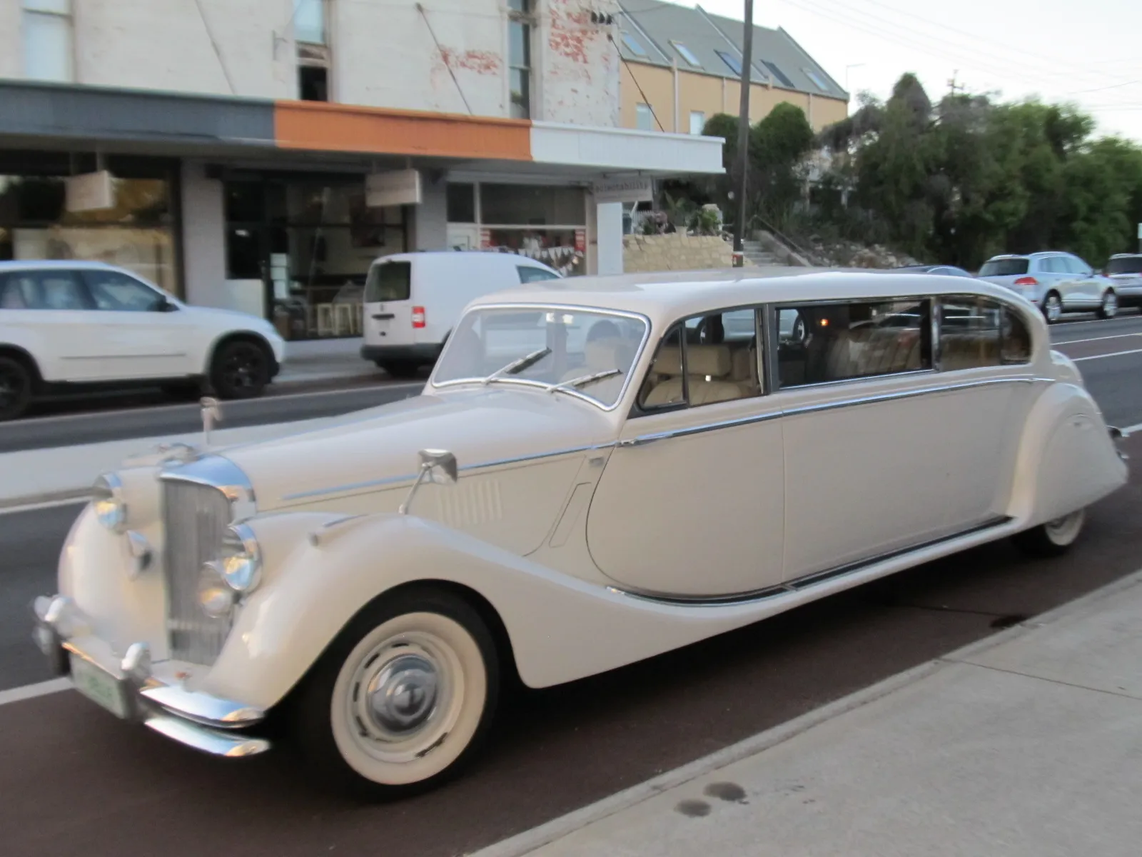 Classic white stretch limousine parked on a city street with older building storefronts in the background.