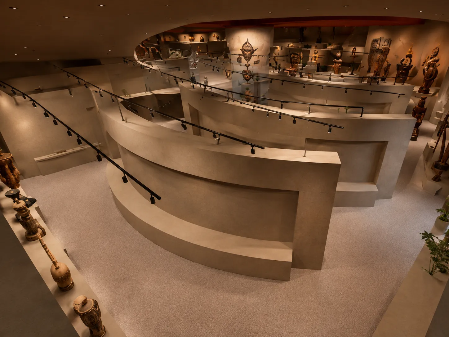 Museum interior with curved beige walls displaying various sculptures and artifacts under focused lighting.