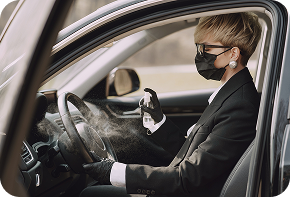 Person wearing black mask and gloves sprays disinfectant inside a car.