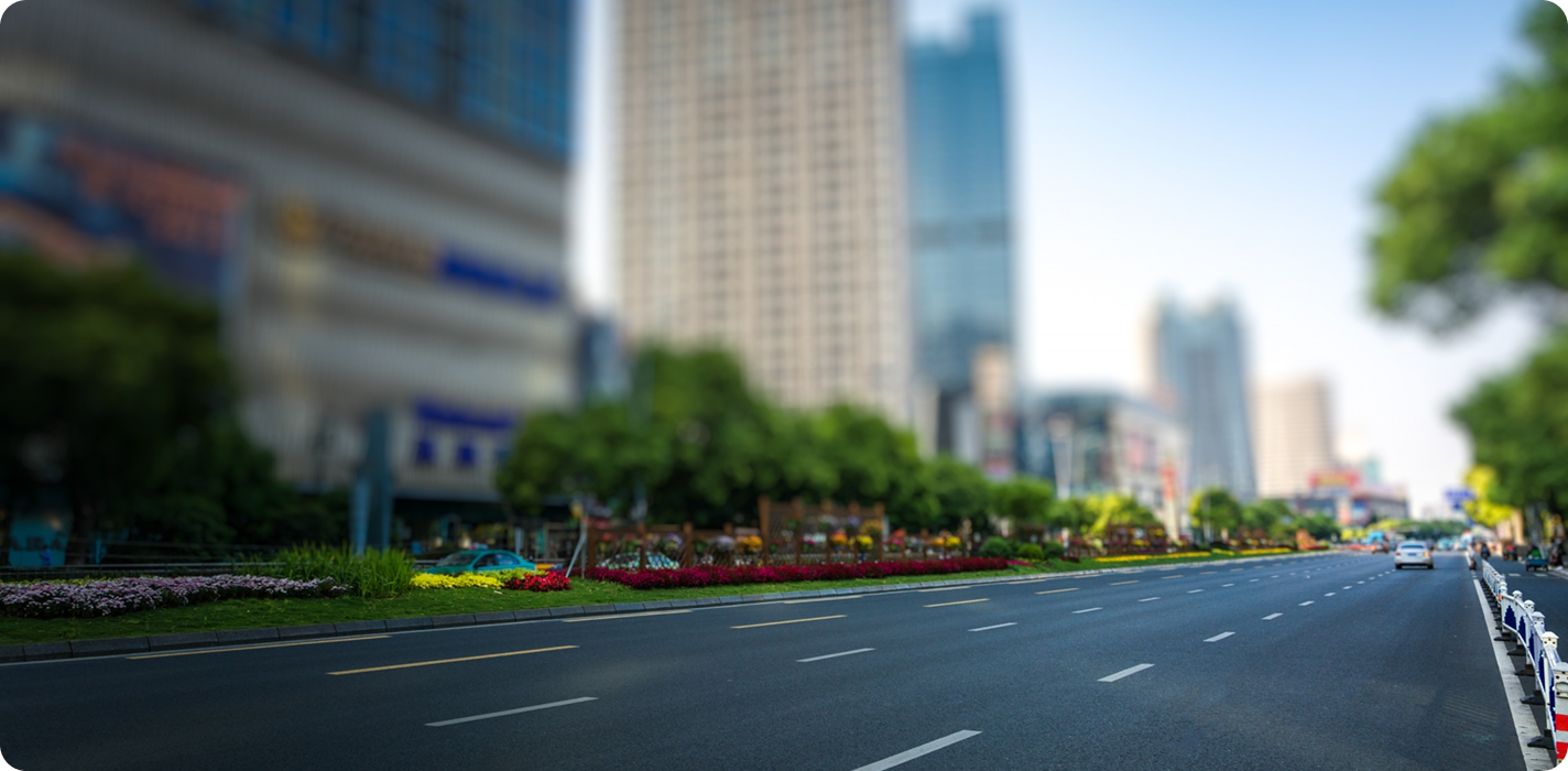 Multi-lane city street with flowerbeds and high-rise buildings under a clear blue sky.