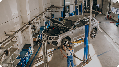 Mechanic inspecting a silver SUV lifted inside a bright, spacious auto repair garage.