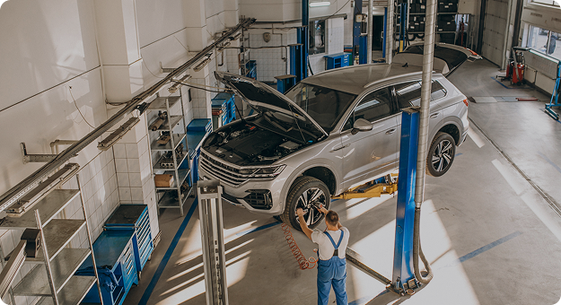 Mechanic in blue overalls servicing a silver SUV lifted in a bright, clean auto repair shop.