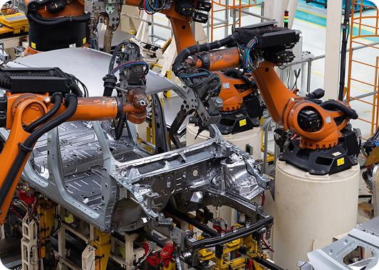 Robotic arms assembling a silver car frame on an automotive factory line.
