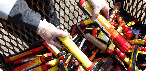 Gloved hands holding yellow and red flare canisters over a mesh container filled with similar canisters.