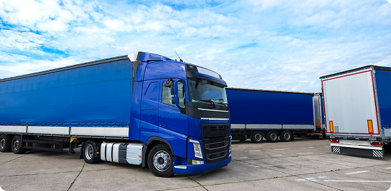 Blue semi-trailer trucks parked on a concrete lot under a cloudy sky.