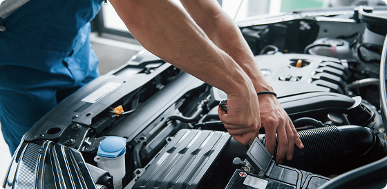 Mechanic working on a car engine under the hood in a well-lit garage.