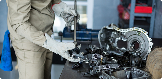 Mechanic wearing gloves repairs automotive gearbox parts on a workbench in a workshop.