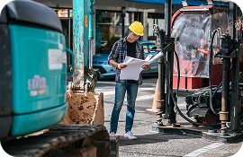 Construction worker in yellow helmet reviewing plans on an urban construction site.