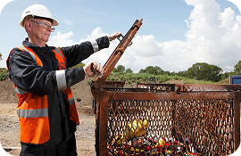 Man in safety helmet and vest operating a machine sorting recyclable plastic bottles outdoors.