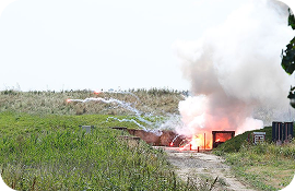 Explosion with smoke and fire near a grassy embankment on a dirt road.