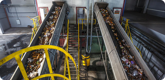 Conveyor belts carrying mixed waste in a recycling or waste sorting facility with yellow railings.