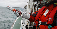 Person in red safety gear holding a fire extinguisher on a boat near the water.
