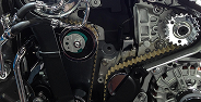 Close-up of a motorcycle engine chain and sprocket with metal components and wires.