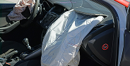 Deployed airbag in a red car's front passenger seat with door open and visible interior.
