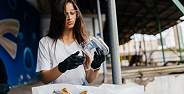 Woman wearing gloves and glasses examining a transparent bottle at a recycling center.