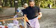 Man and child putting plastic bottles into a trash bin outdoors in a park.