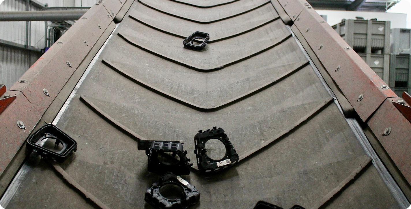 Black plastic parts scattered on an angled industrial conveyor belt inside a warehouse.