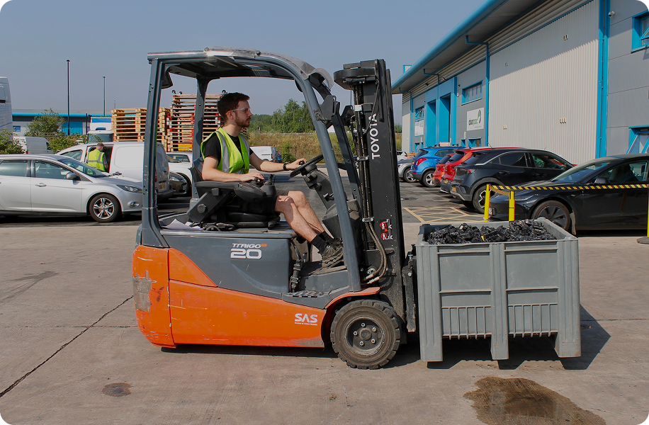 Man in safety vest operating an orange Toyota forklift carrying a large crate outdoors.