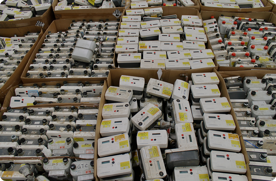 Many old electric meters stacked inside cardboard boxes in a storage area.