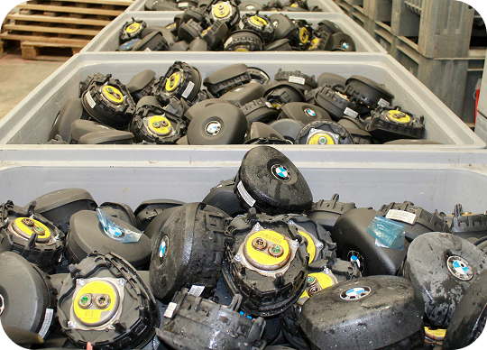 Bins filled with black BMW steering wheel airbag modules in a warehouse setting.