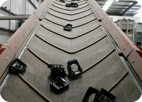 Conveyor belt moving black plastic automotive parts upward inside an industrial factory.