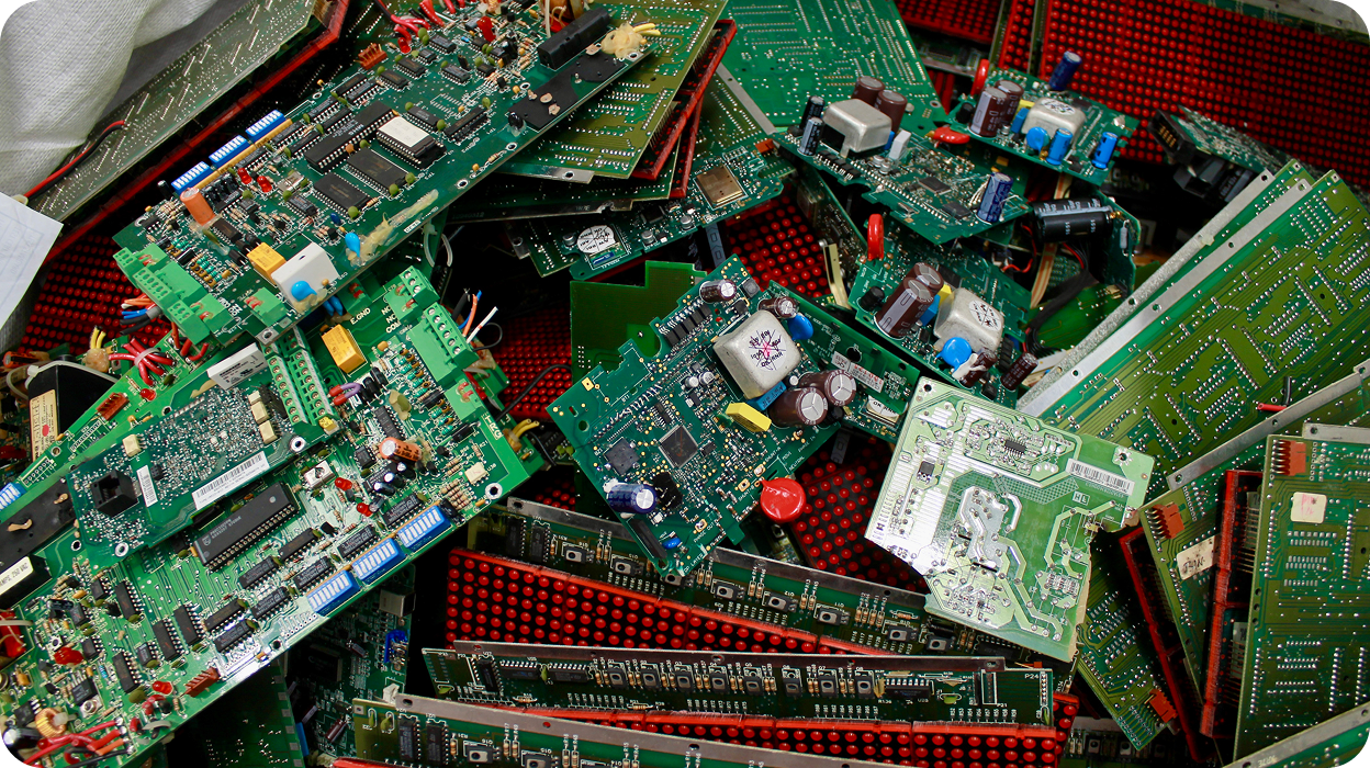 Pile of green printed circuit boards with various electronic components on a red surface.