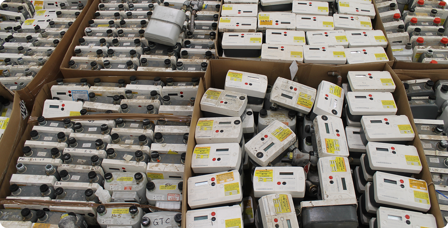 Boxes filled with numerous old utility meters with labels, dials, and red and black buttons.