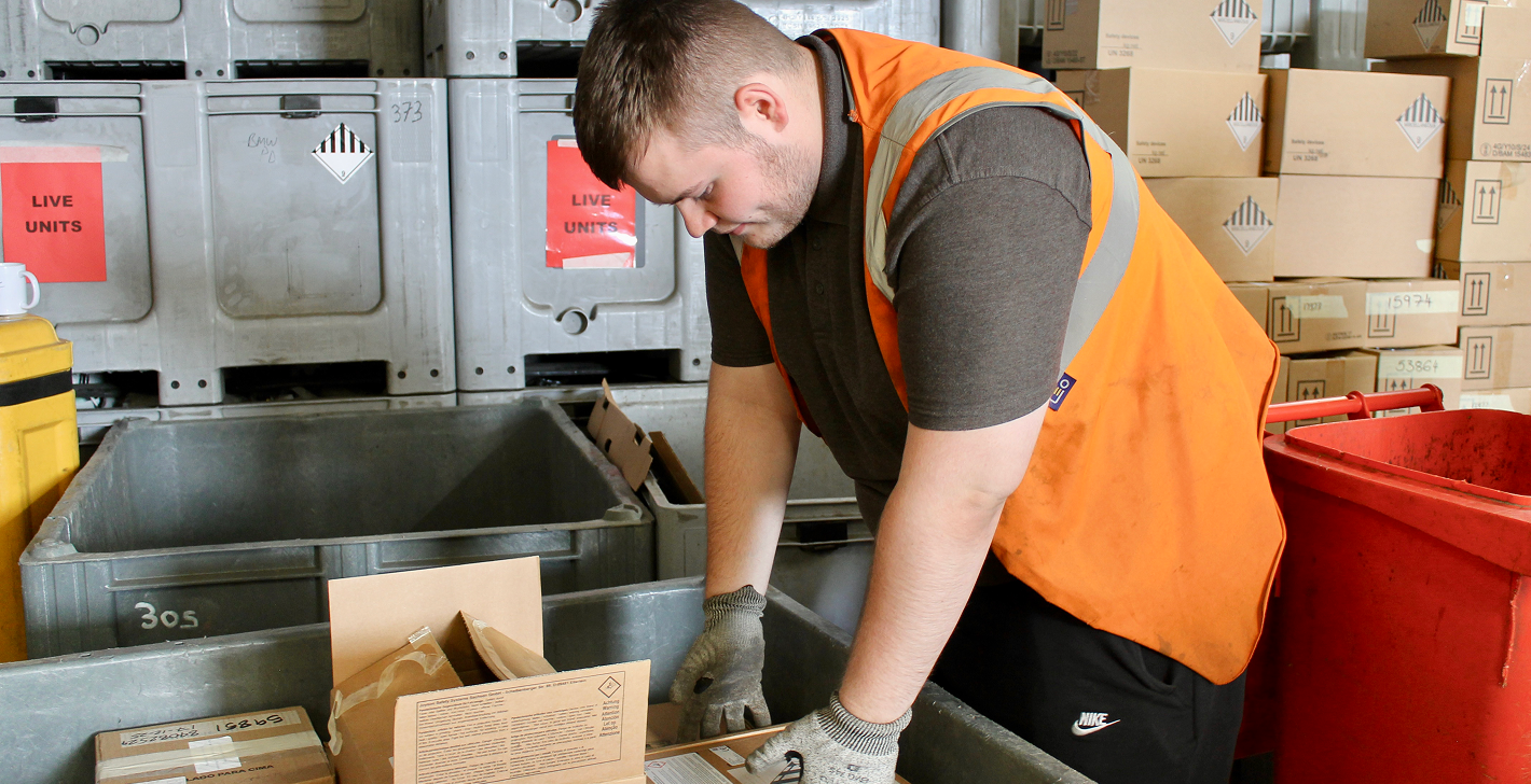 Worker in orange safety vest handling boxes in a warehouse with labeled crates and cartons.